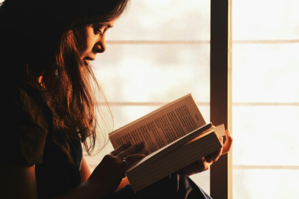 A woman engrossed in reading a book by a sunlit window creates a serene atmosphere. vastu