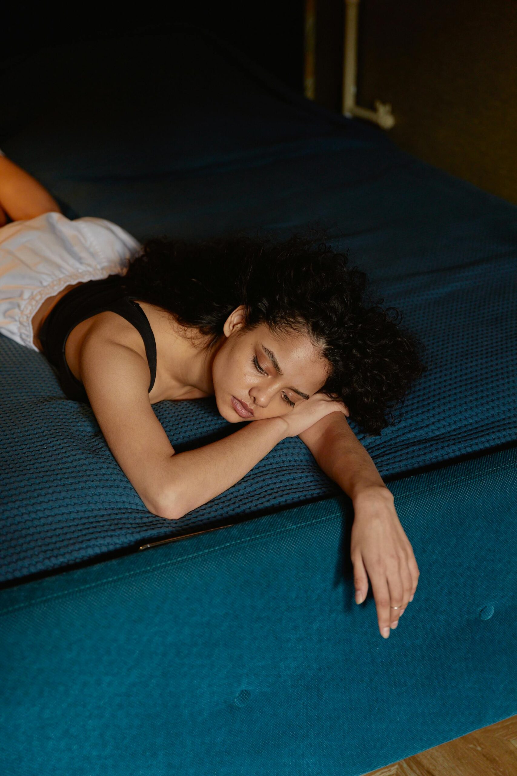 Thoughtful woman with curly hair lying on bed, expressing contemplation and calmness.